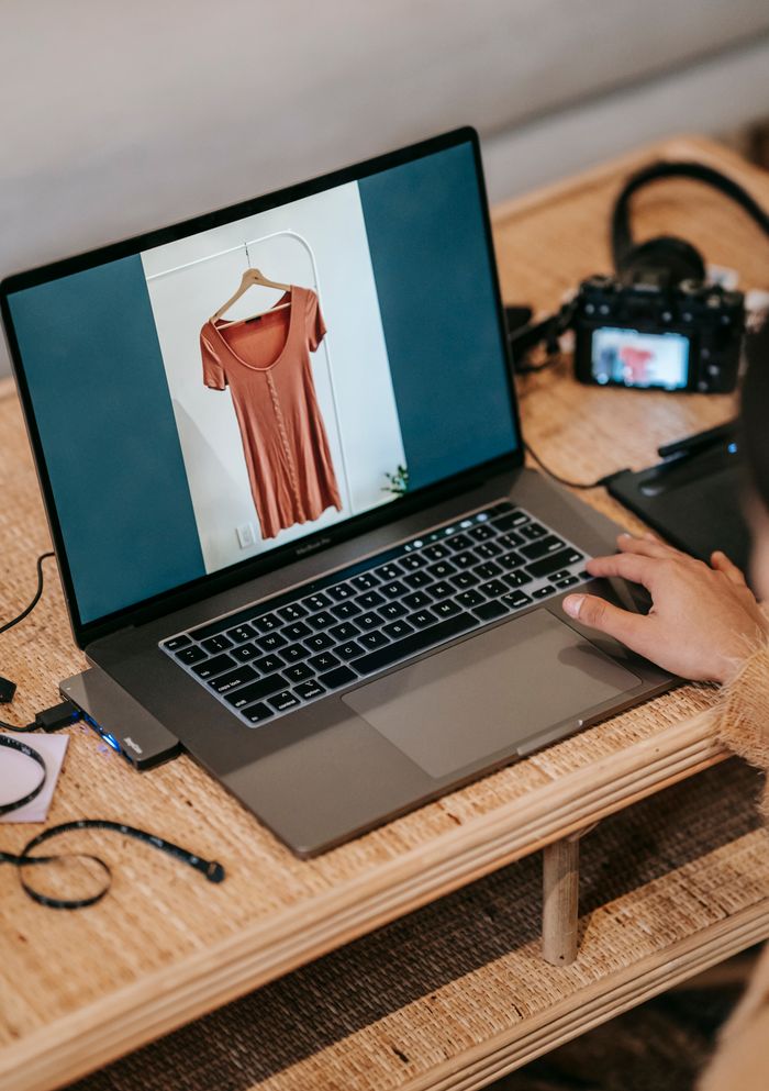 From above of crop anonymous freelancer demonstrating photography of clothes on netbook screen at table